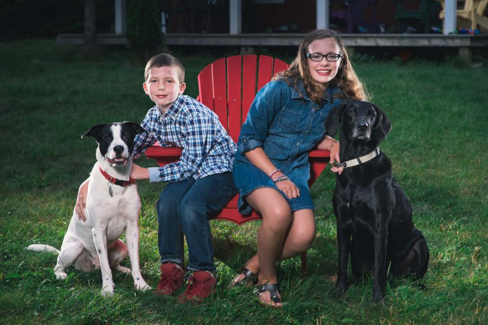 Two childrens pose with their family dogs.