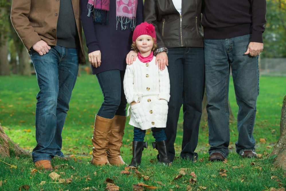 A young girl poses with all the adults, but the adults have their upper bodies cropped out of the frame as to accentuate the height difference between the young girl and her parents.