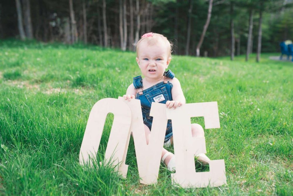A baby celebrates her very first birthday by posing with big wooden letters that spell out the number one.