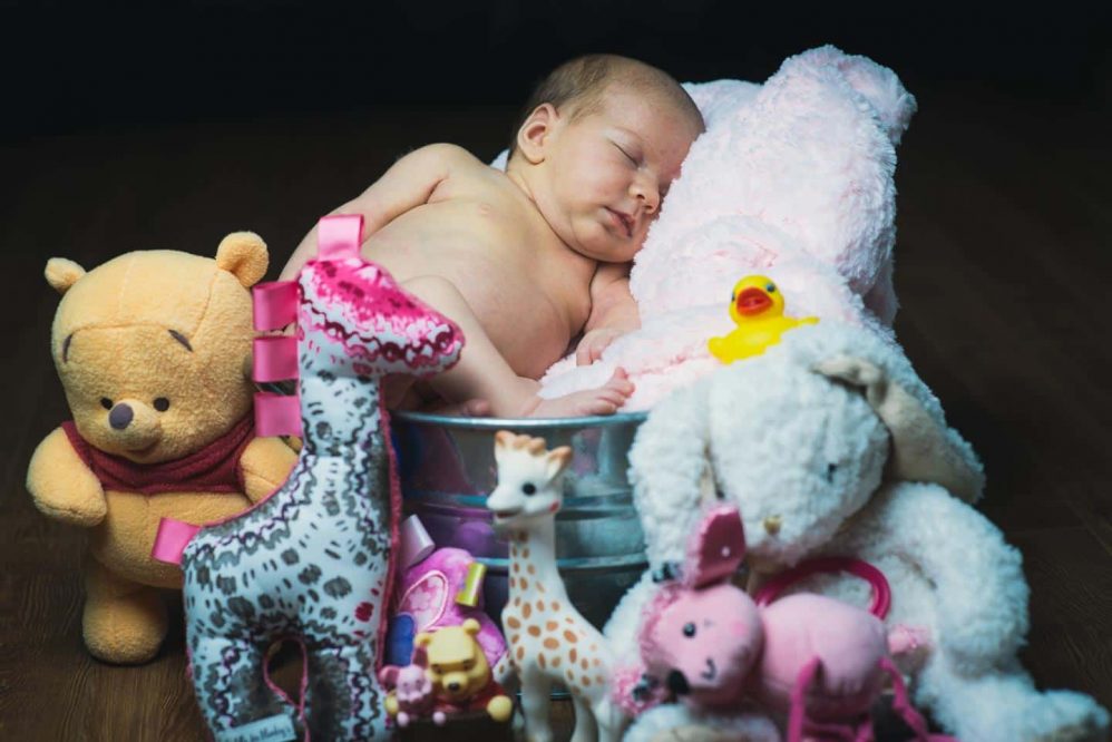 A young baby girl poses with all her stuffed animals.