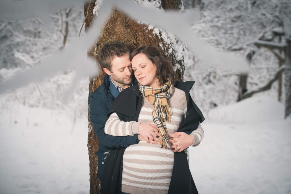 A couple embrace near an old tree with winter all around.