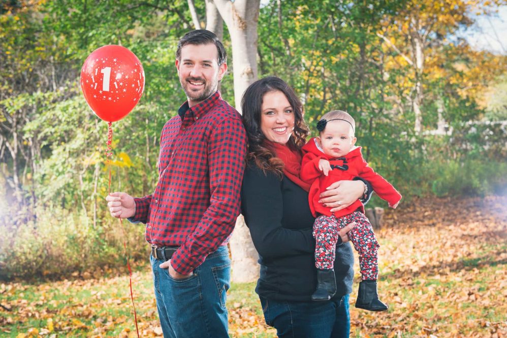 A famiy's first photo features a fun dad holding a balloon while mom holds the newborn.