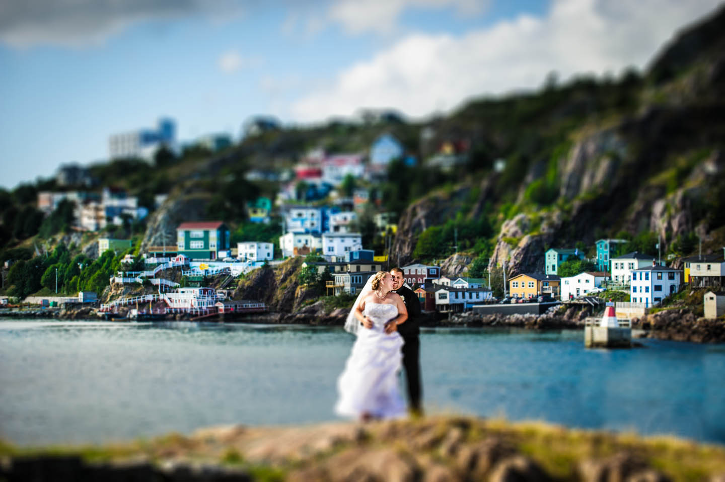 With the colorful outer battery of St. John's a bride and groom embrace on the rocks for a wedding photo.
