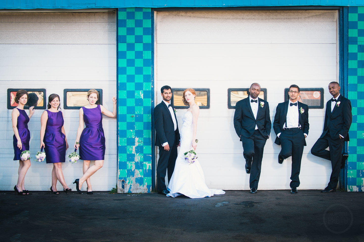 Against the colorful paint of a 1960s style garage door a bridal party poses.