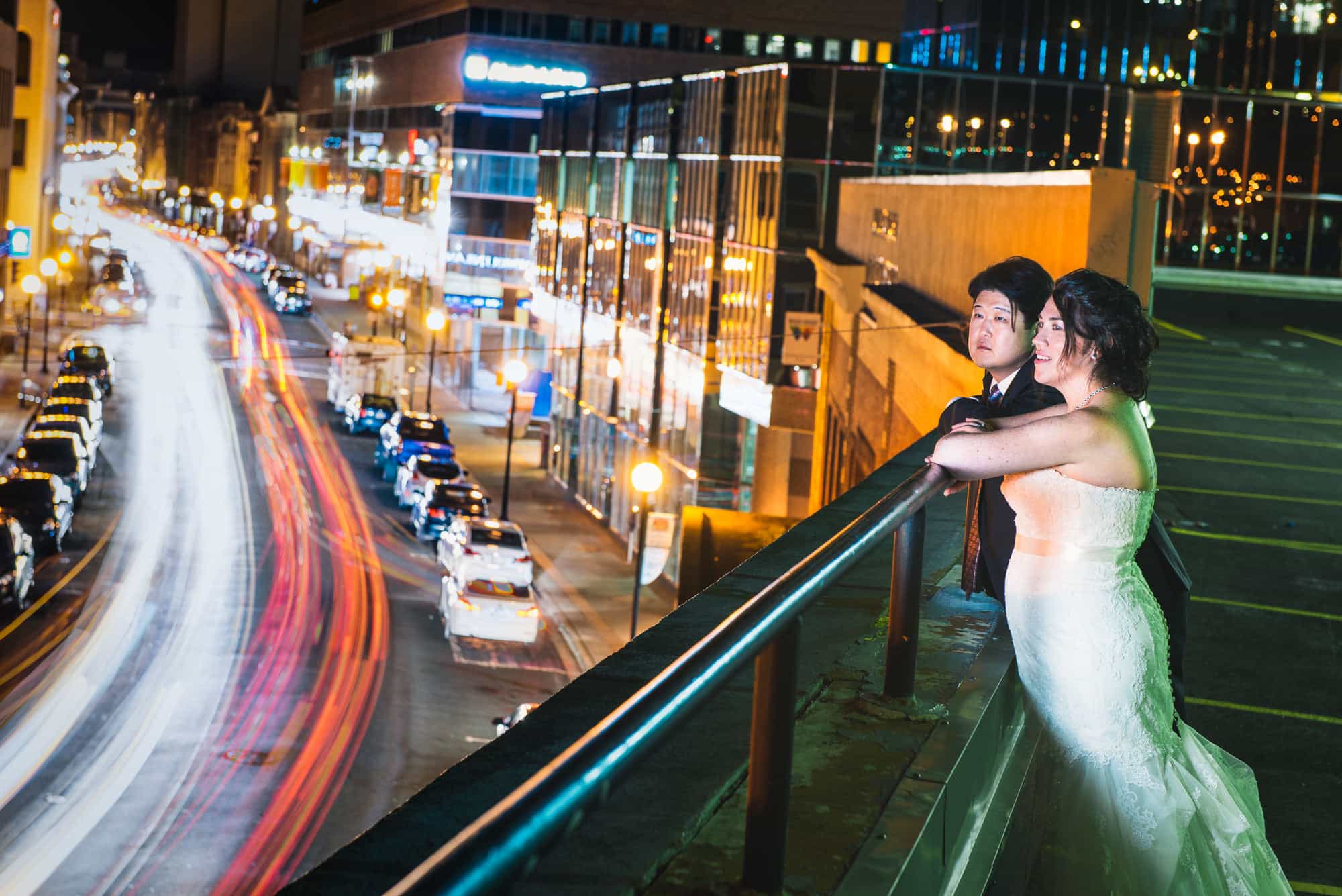 In a colorful night photograph a wedding couple look out over a the motion of Water Street in St. John's, Newfoundland