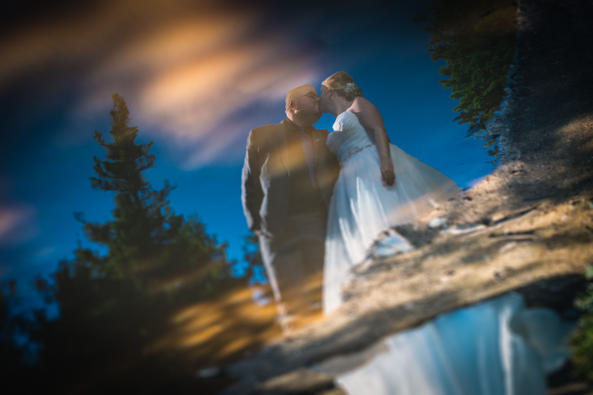 A wedding couple in Newfoundland kiss while the reflection is photographed in a puddle