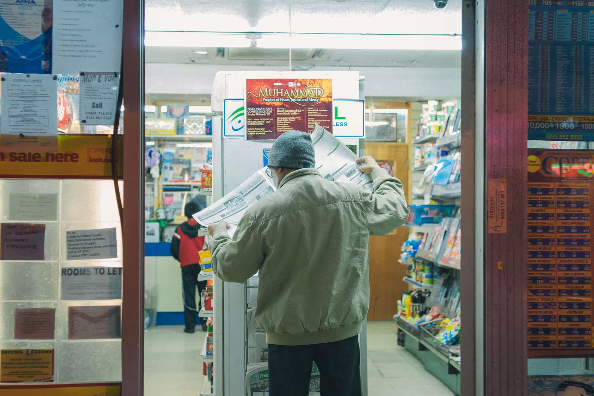 Manchester, England - In this street photograph a man reads the newspaper in a shop on Curry Mile in south Manchester.