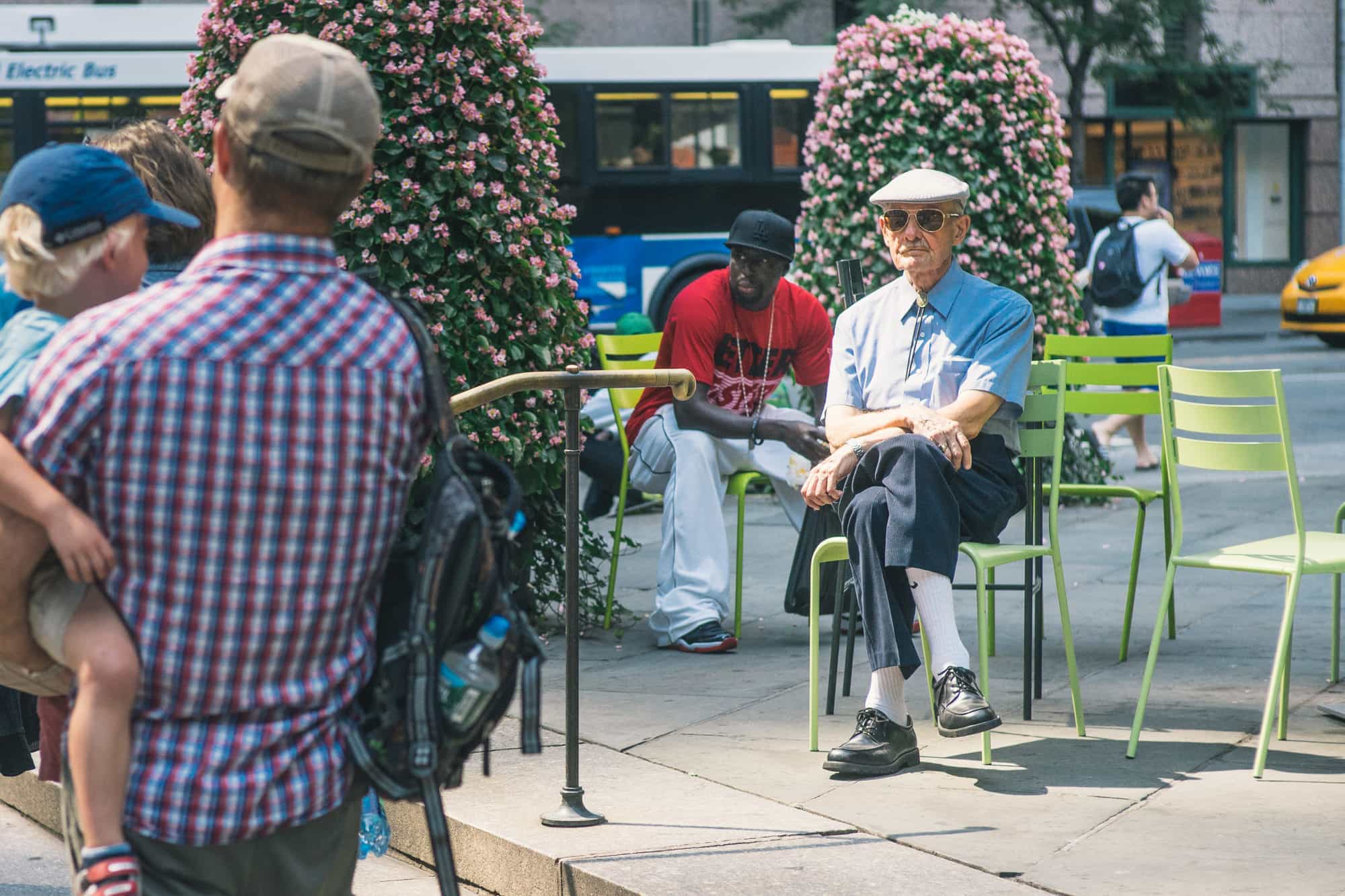 A well dressed man sits on a park chair in Manhattan in this NYC street photograph.