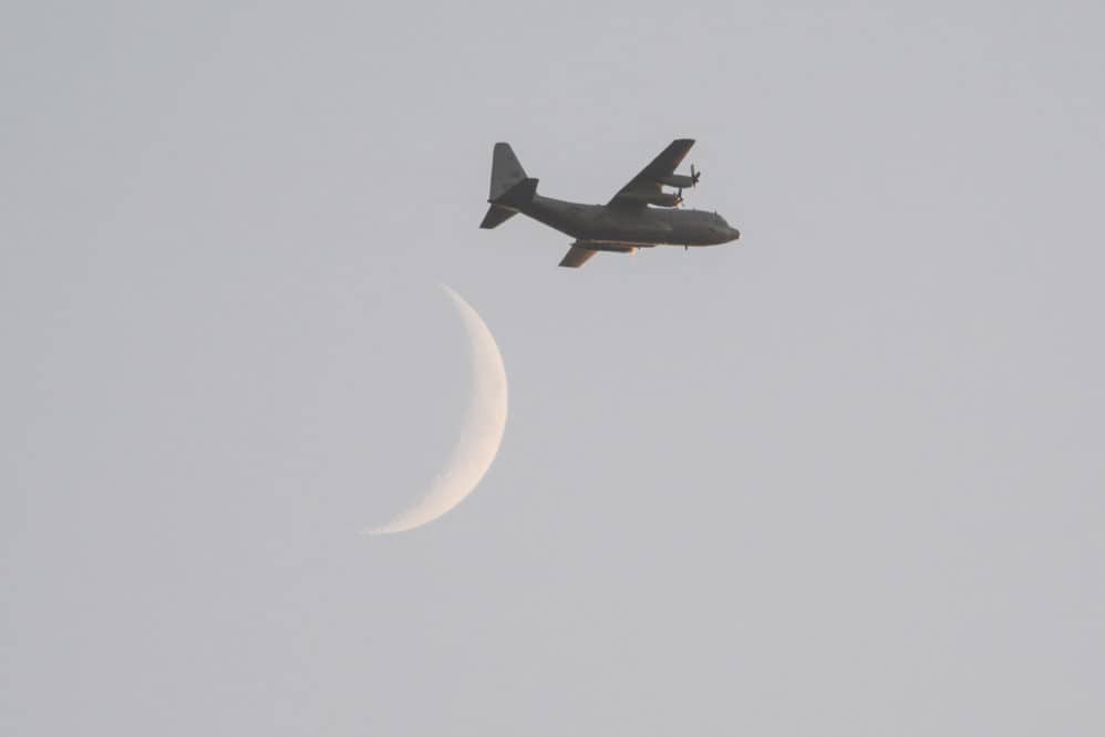 A C130 flies with the moon in the background.