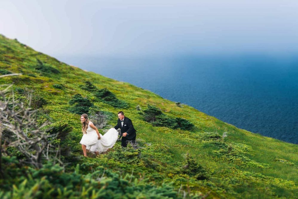 A groom helps his bride up over the brush in scenic Newfoundland along the coast line.