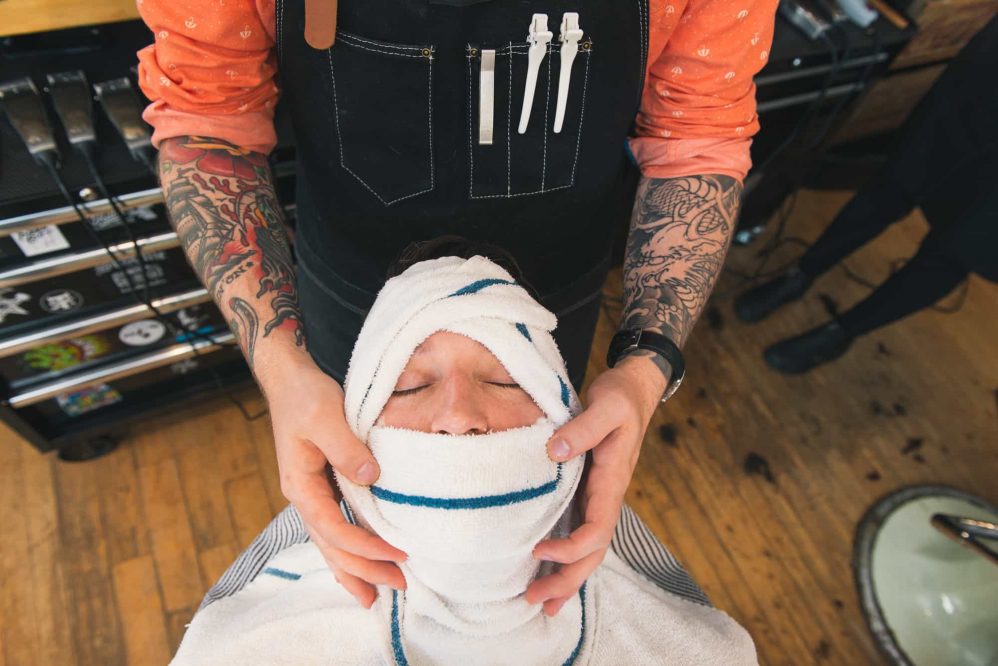 The groom of a wedding has his face steamed with hot face clothes prior to his big moment.