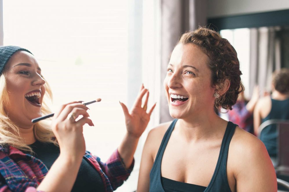 The bride smiles while having her makeup done.