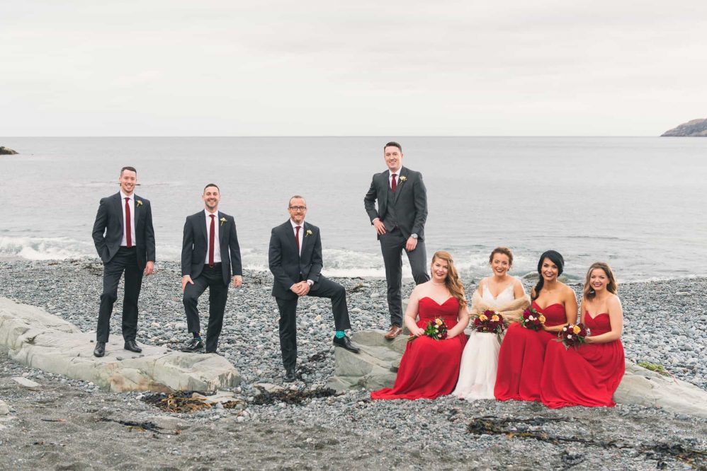 Along a beach, a bridal party poses for a photograph.