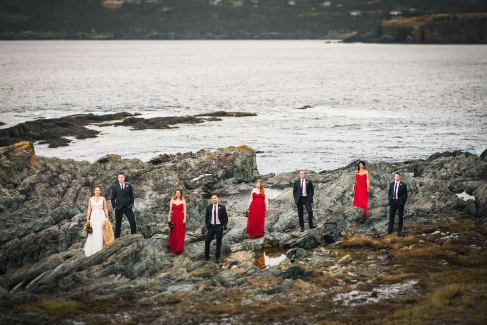 A wedding bridal party poses for the camera along a rugged and rocky coastline.