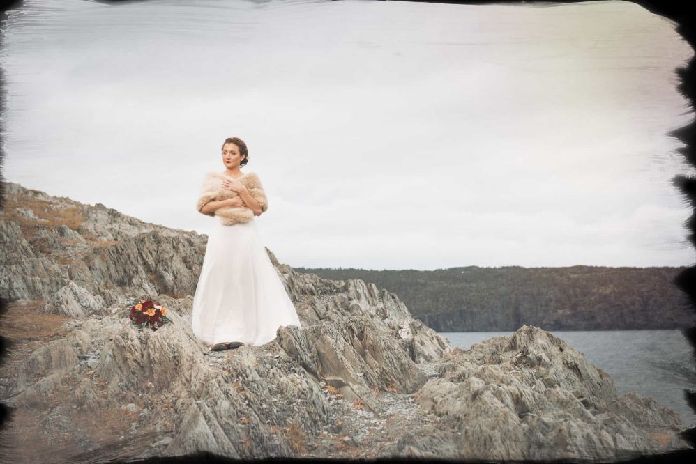 A bride stands along a jagged rockface for a wedding photograph.