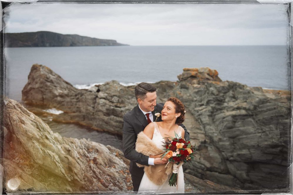 Bride and groom pose for picture on the rocks.