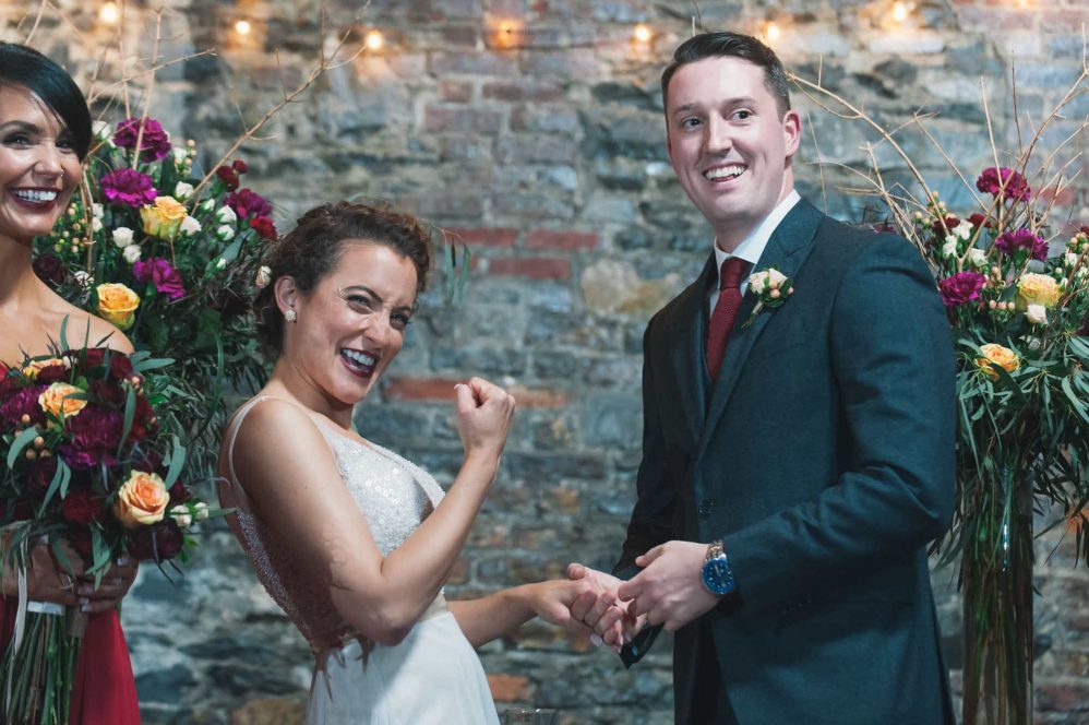 A bride candidly pumps her fist after having the wedding ring put on her finger.