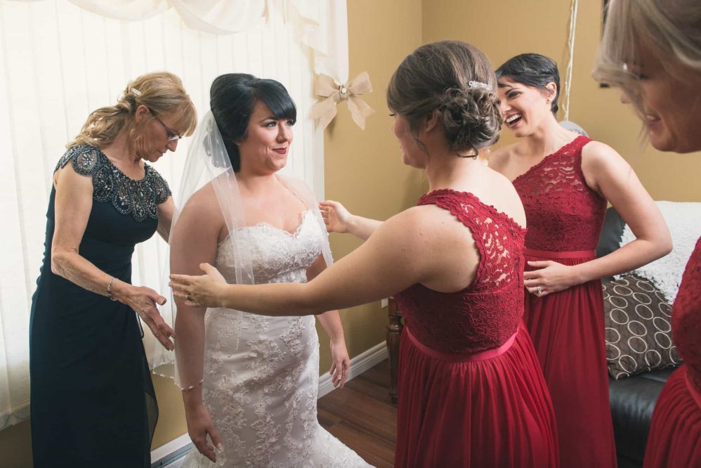 The bride's mom and her bridesmaids prepare her dress for the wedding.