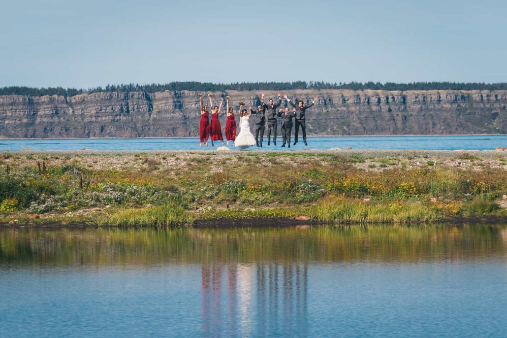 The entire bridal party is seen jumping along the coast line with their reflections in the water.