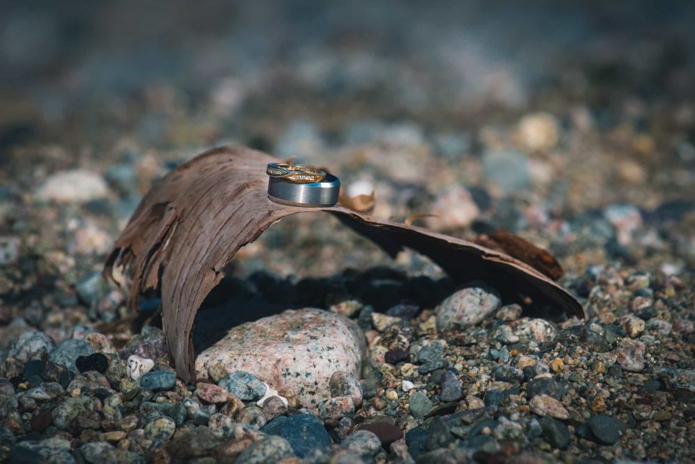 The wedding rings are placed on piece of tree bark along the beach rocks.
