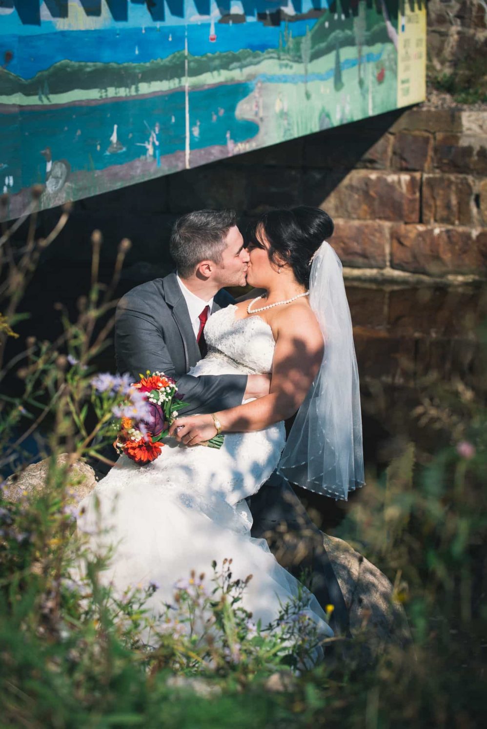 The bride and groom kiss near a river and the bridge.