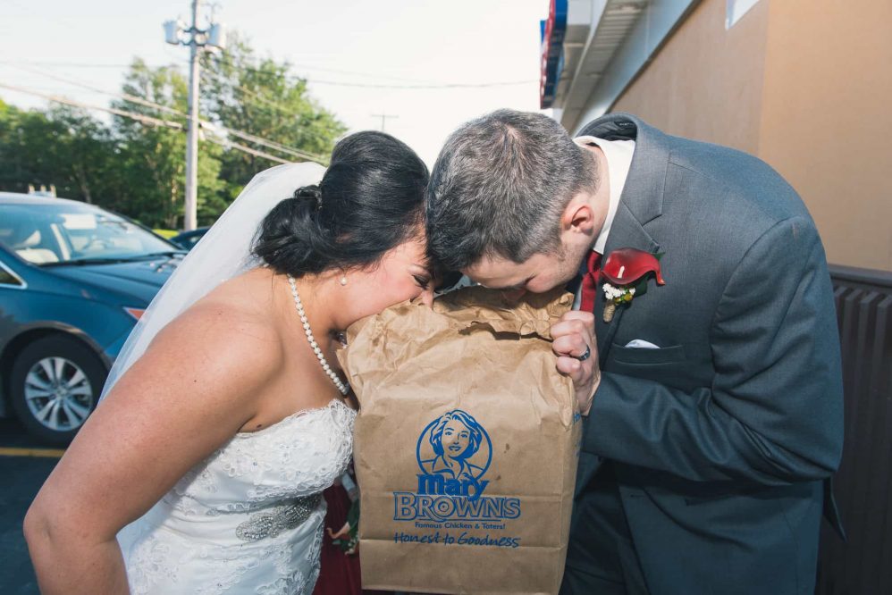 The bride and groom inhale the scent of a bag of fast food.