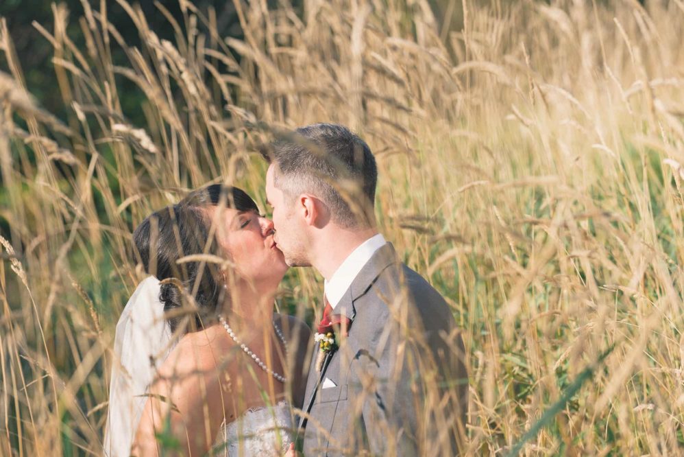 A bride and groom steal a kiss amongst the tall grass.