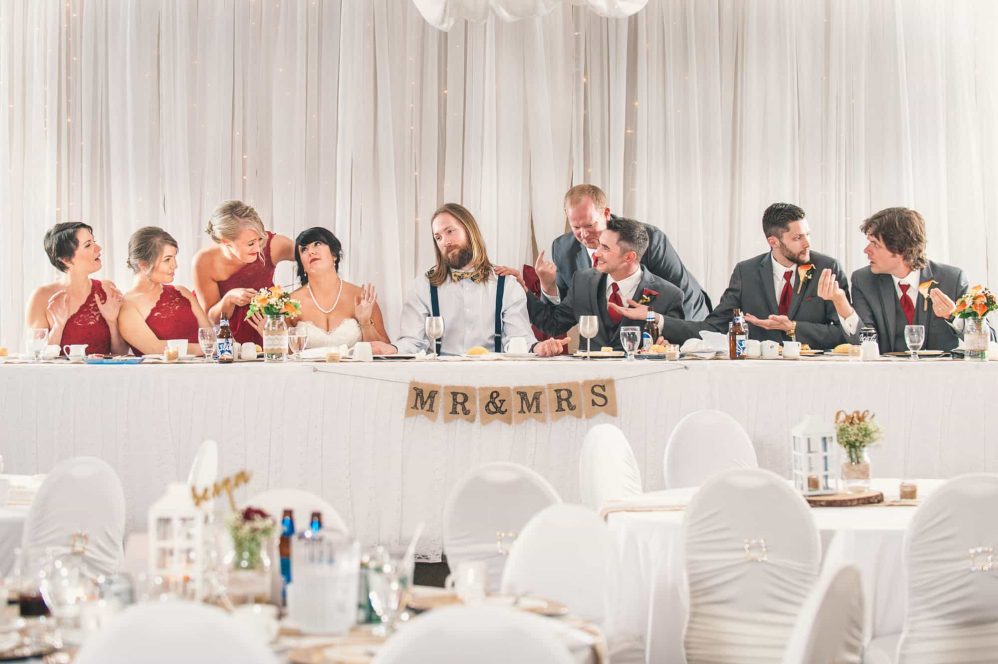 An entire bridal party poses for a funny photograph emulating leonard da vinci's last supper painting.