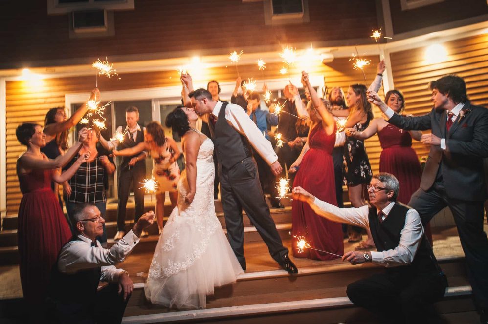 Friends and family hold sparklers while the bride and groom kiss in the glow of the light.
