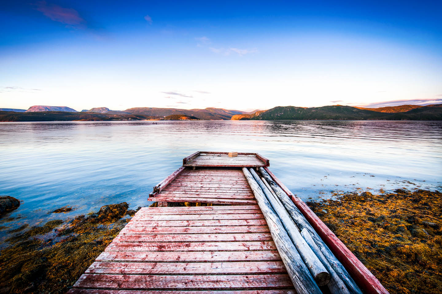 This is a photograph of an old wharf in Curzon Village which lays at the entrance to Bonne Bay in Newfoundland. In the distance you can see Rocky Harbour and Norris Point. If you’re looking for a colorful photo of Newfoundland, then you’ve found it. The pinks and blue hues together combine for some awesome eye candy.